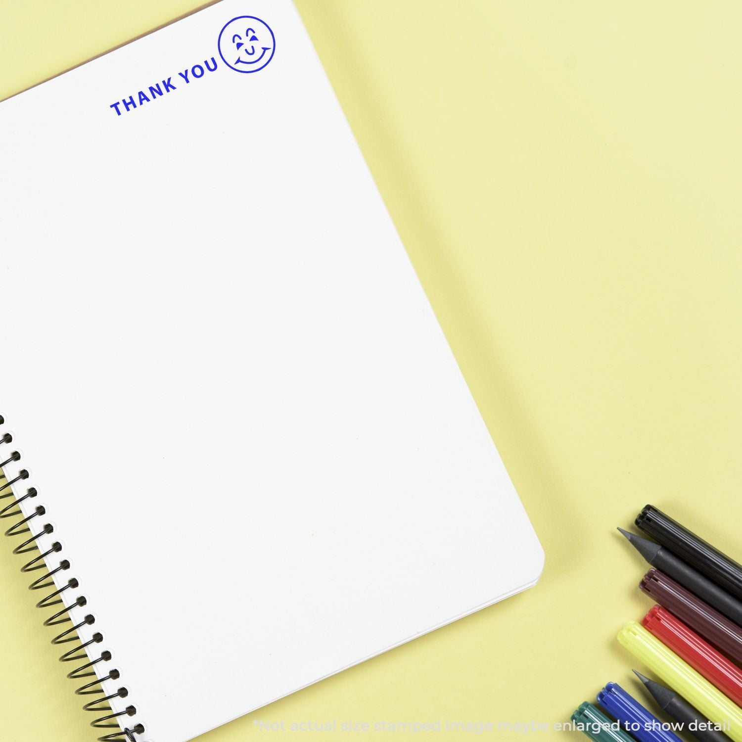 White spiral notebook with Thank You stamp and colorful markers on a yellow background.