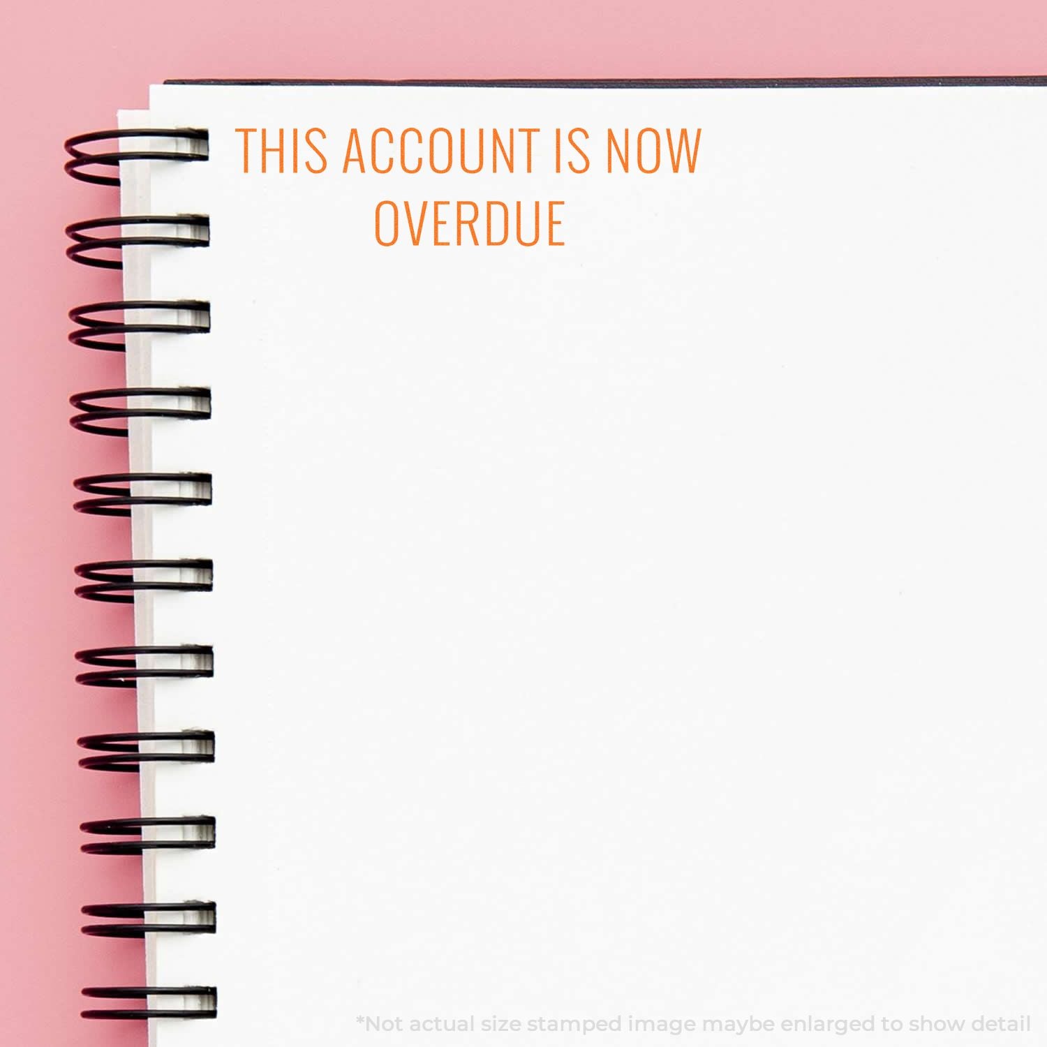 Notebook page with This account is now overdue text, billing reminder concept, white spiral notebook on pink background.