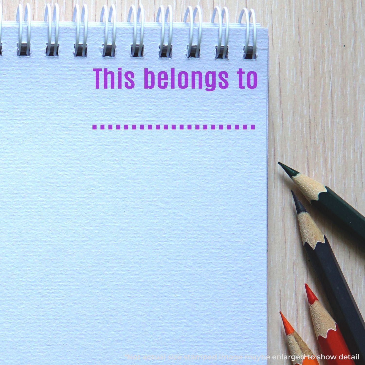 Spiral notebook with This belongs to text and colored pencils on a wooden desk, blank copy space for school or office branding.