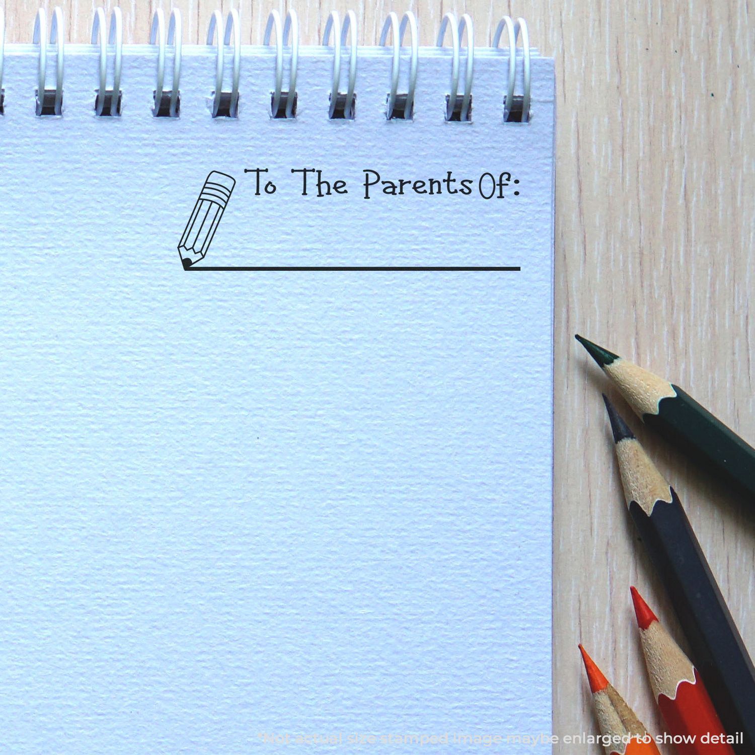 Blank spiral notebook page with To The Parents Of: text and pencil graphic on a wooden desk with colored pencils.