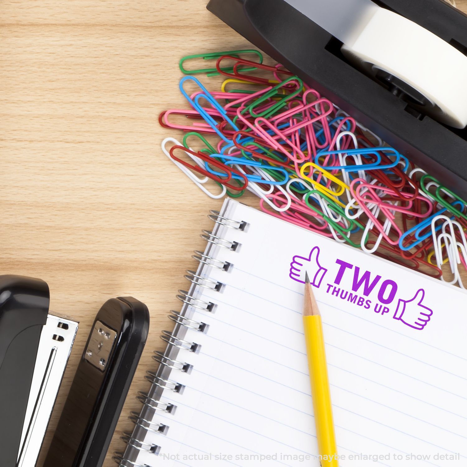 Colorful paper clips, spiral notebook, and pencil on office desk with two thumbs up stamp.