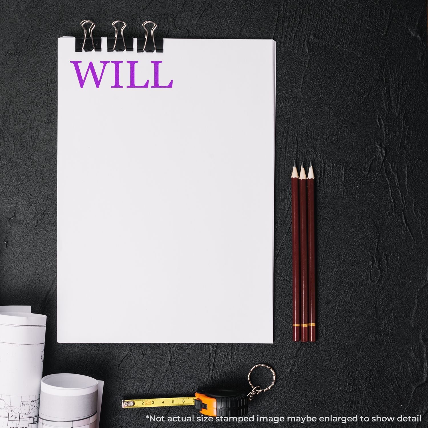 Will word written on a blank notepad with pencils, measuring tape, and rolled blueprints on a black desk.