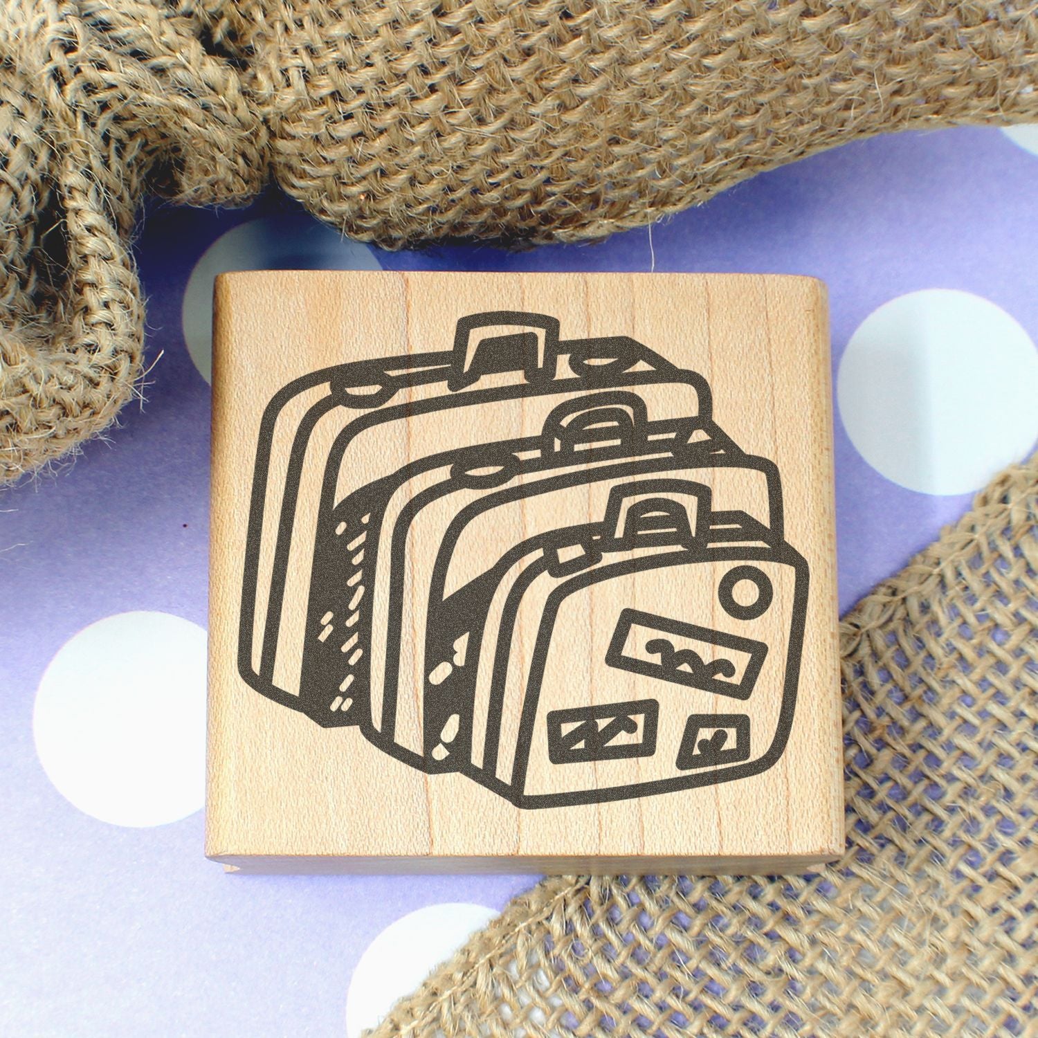Wooden suitcase stamp block on purple polka dot background with burlap texture, travel-themed craft design.