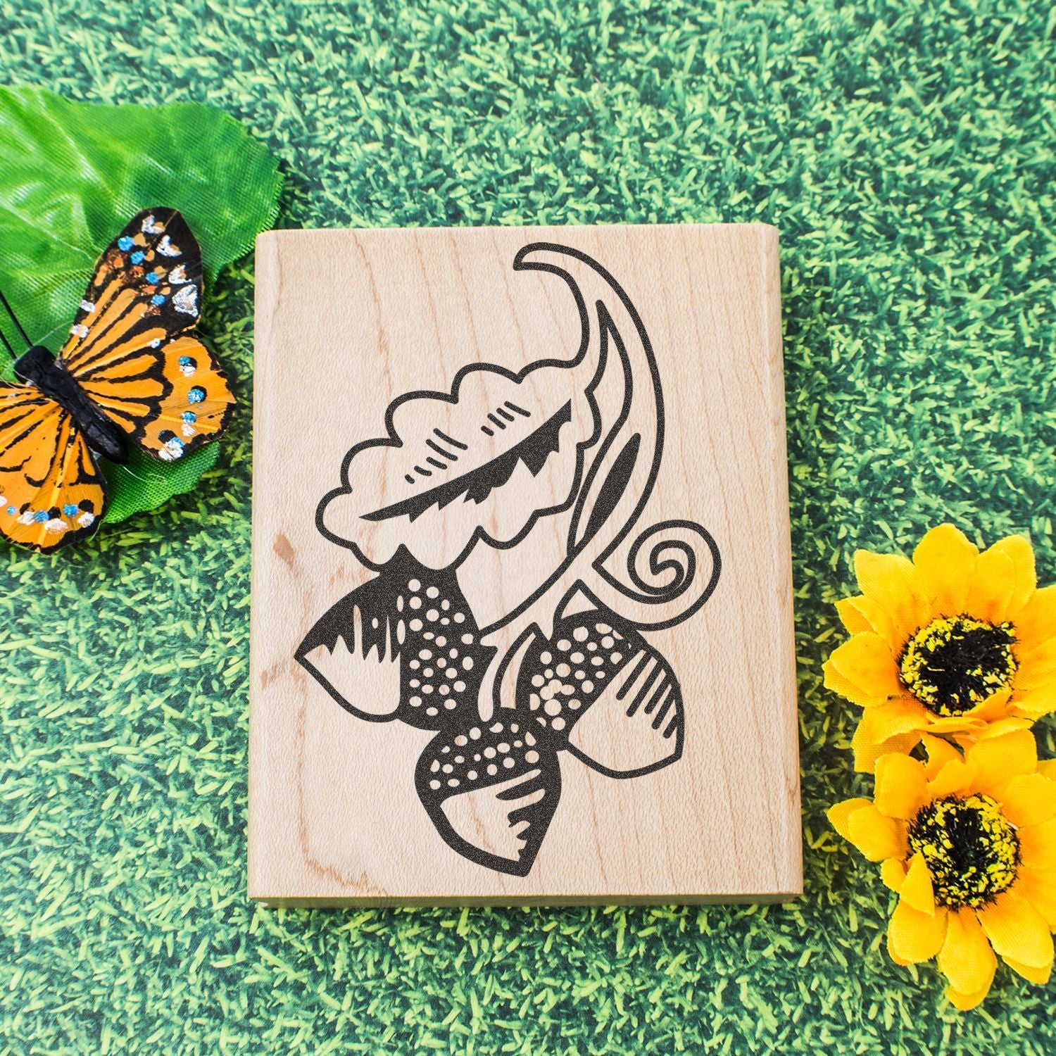Laser engraved wooden block with floral butterfly design on green grass background, decorated with butterfly and yellow flowers.