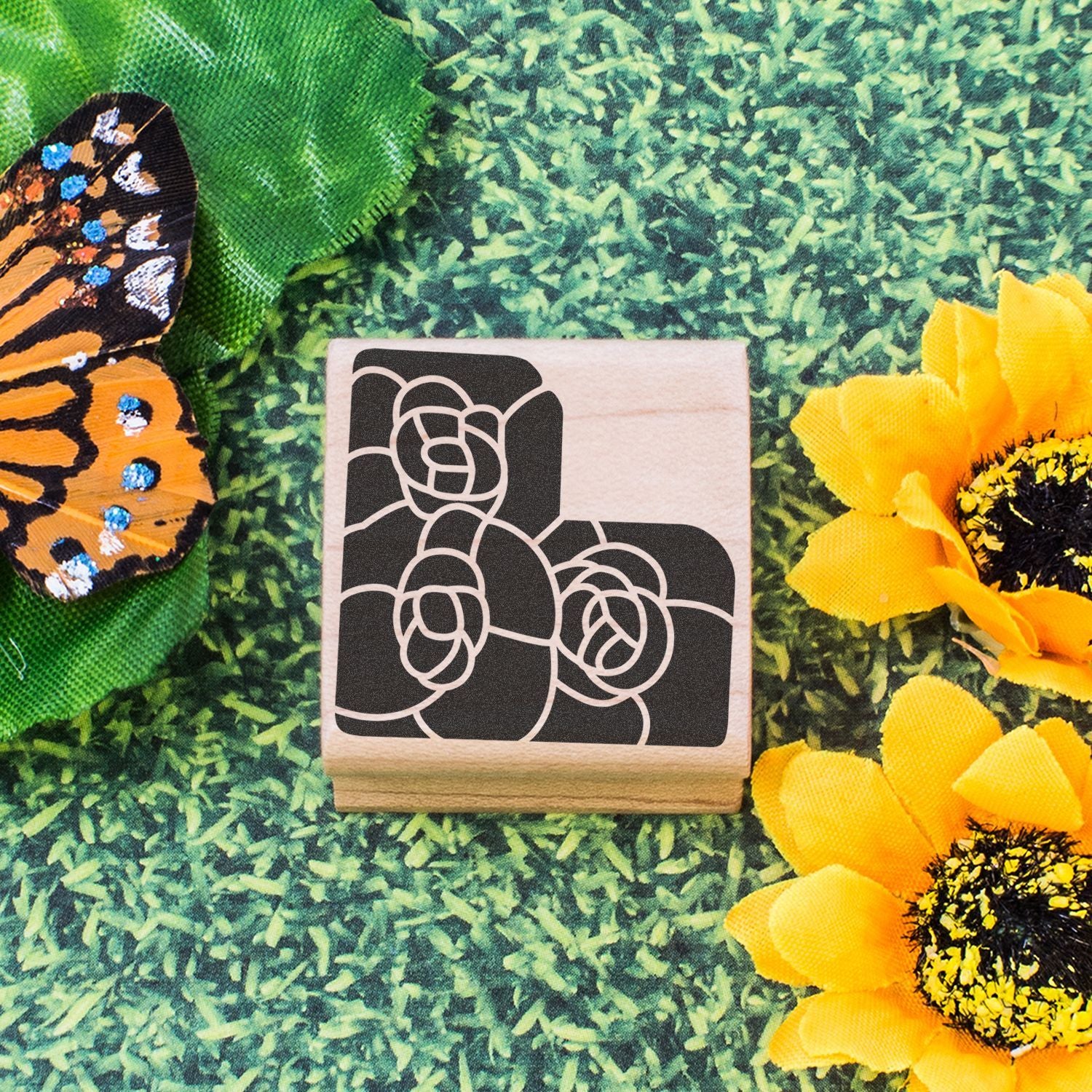 Wooden floral rubber stamp with butterfly wing and sunflower accents on a green garden background