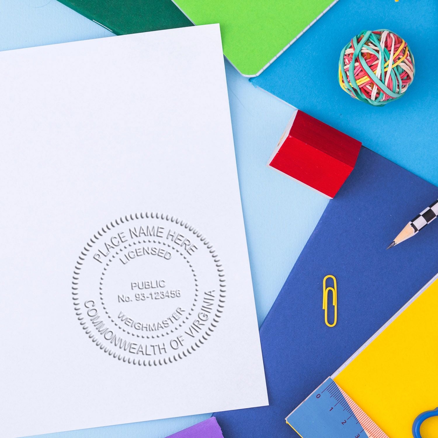 Blank Commonwealth of Virginia notary seal on white paper surrounded by colorful office supplies, notebooks, pencil, paper clip, ruler and rubber band ball.
