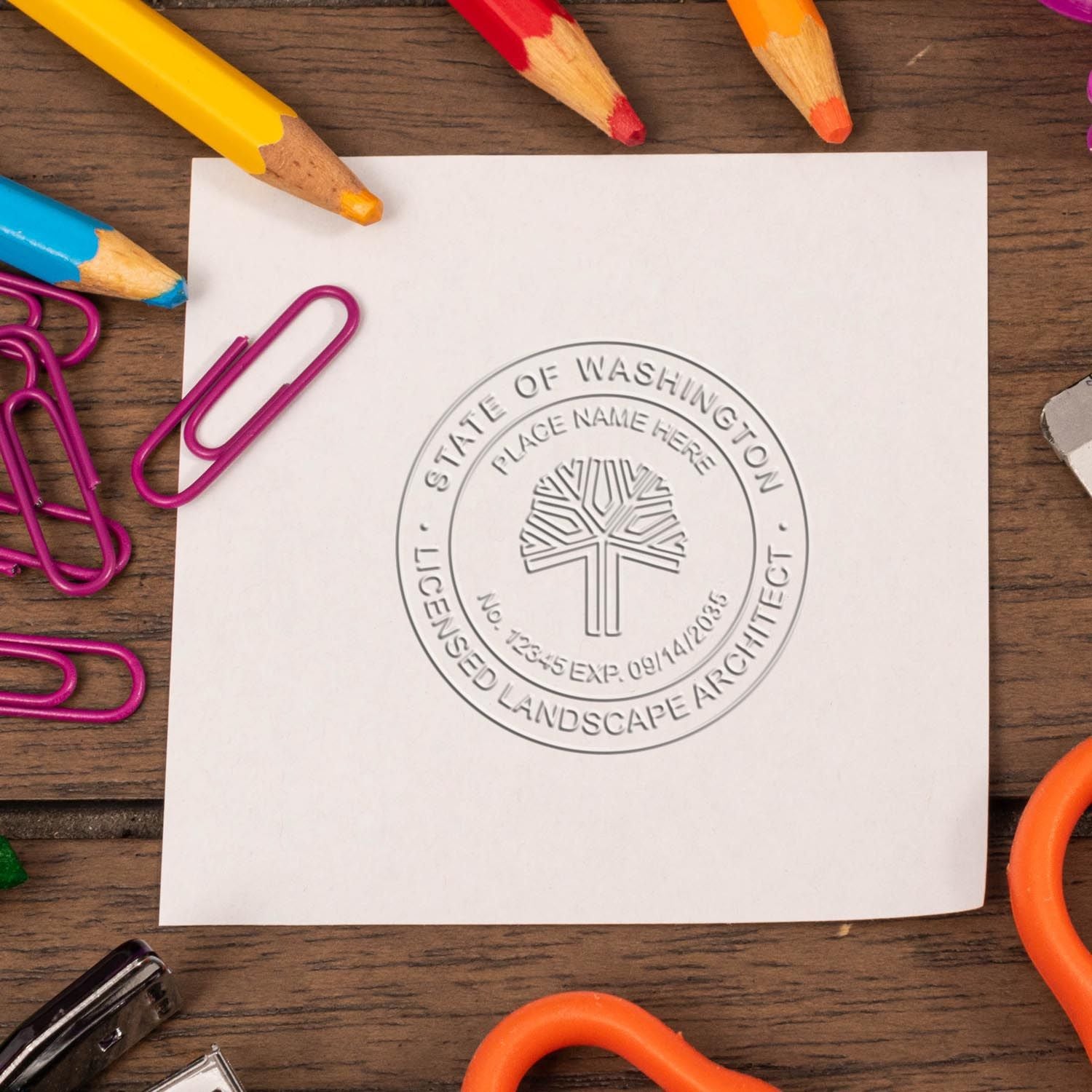 Washington State licensed landscape architect seal on white paper, surrounded by colorful pencils and paperclips on a wooden desk.