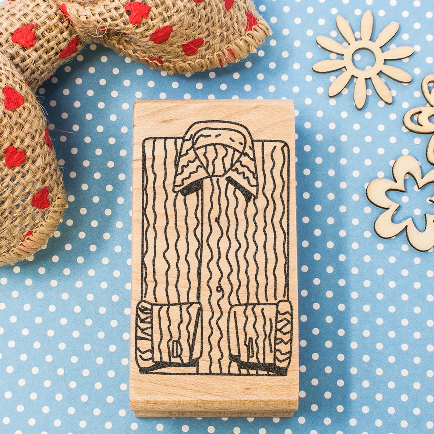 Wooden rubber stamp with hand-drawn folk dress design on blue polka dot background and rustic craft decorations