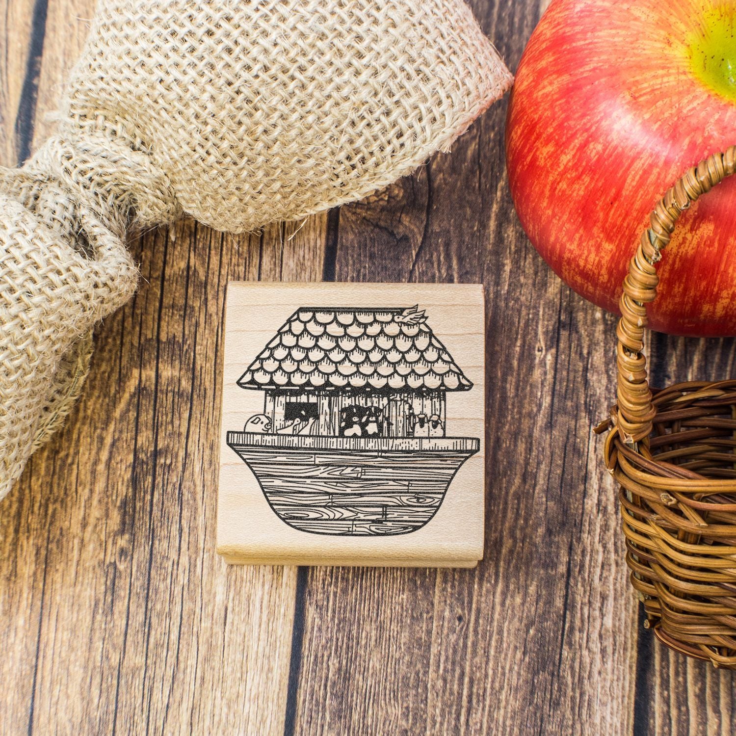 Rustic farmhouse decor with apple, burlap, wicker basket, and wooden stamp featuring a birdhouse illustration on a wood background.