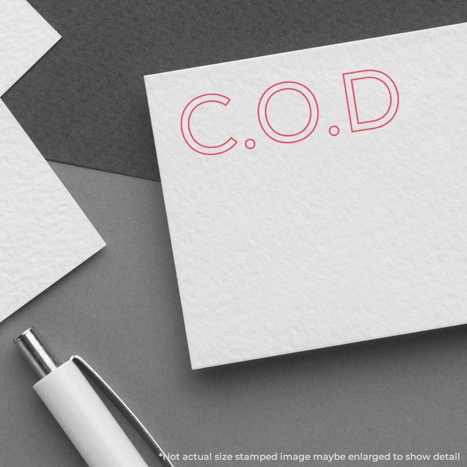 COD cash-on-delivery stamp on white note card with red lettering, placed on dark desk with pen for delivery branding.