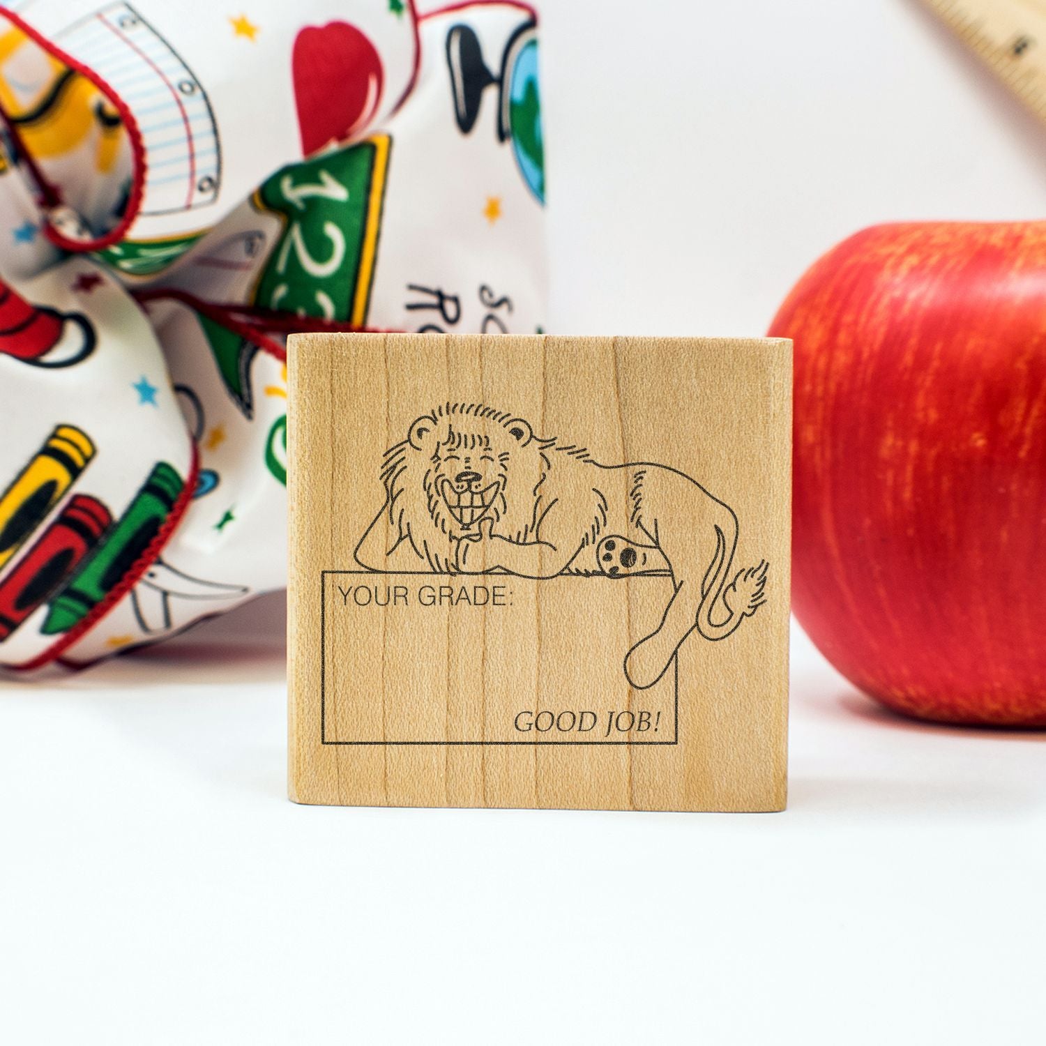 Wooden teacher grading stamp with lion illustration, Your Grade: Good Job! text, and apple school theme background.